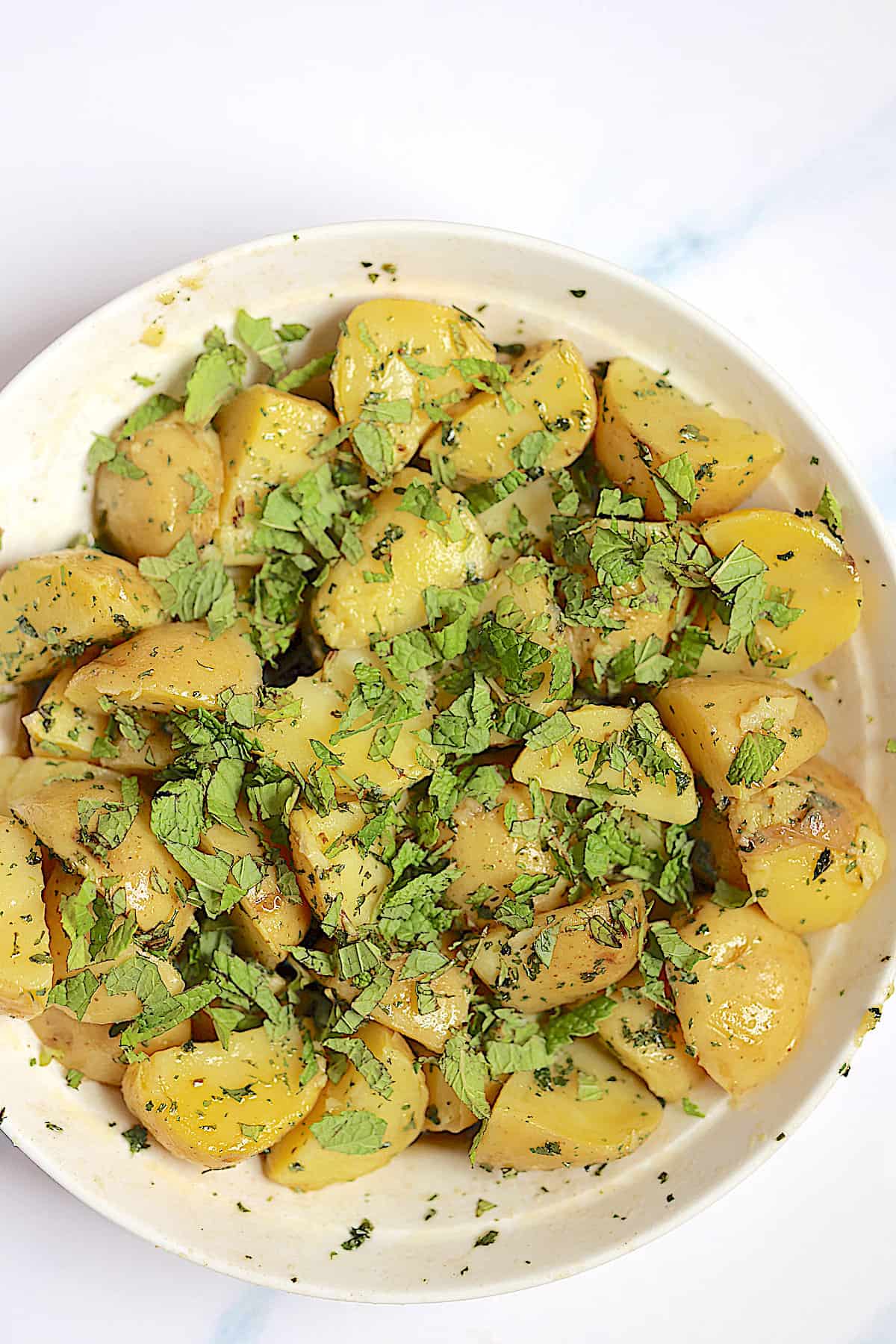 potatoes mixed with mint and parsley in a mixing bowl