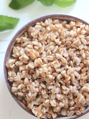 pressure cooked farro in a small bowl surrounded by basil