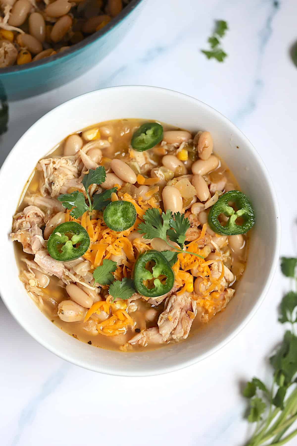 instant pot white chicken chili in a white bowl topped with cheddar cheese and jalapeños