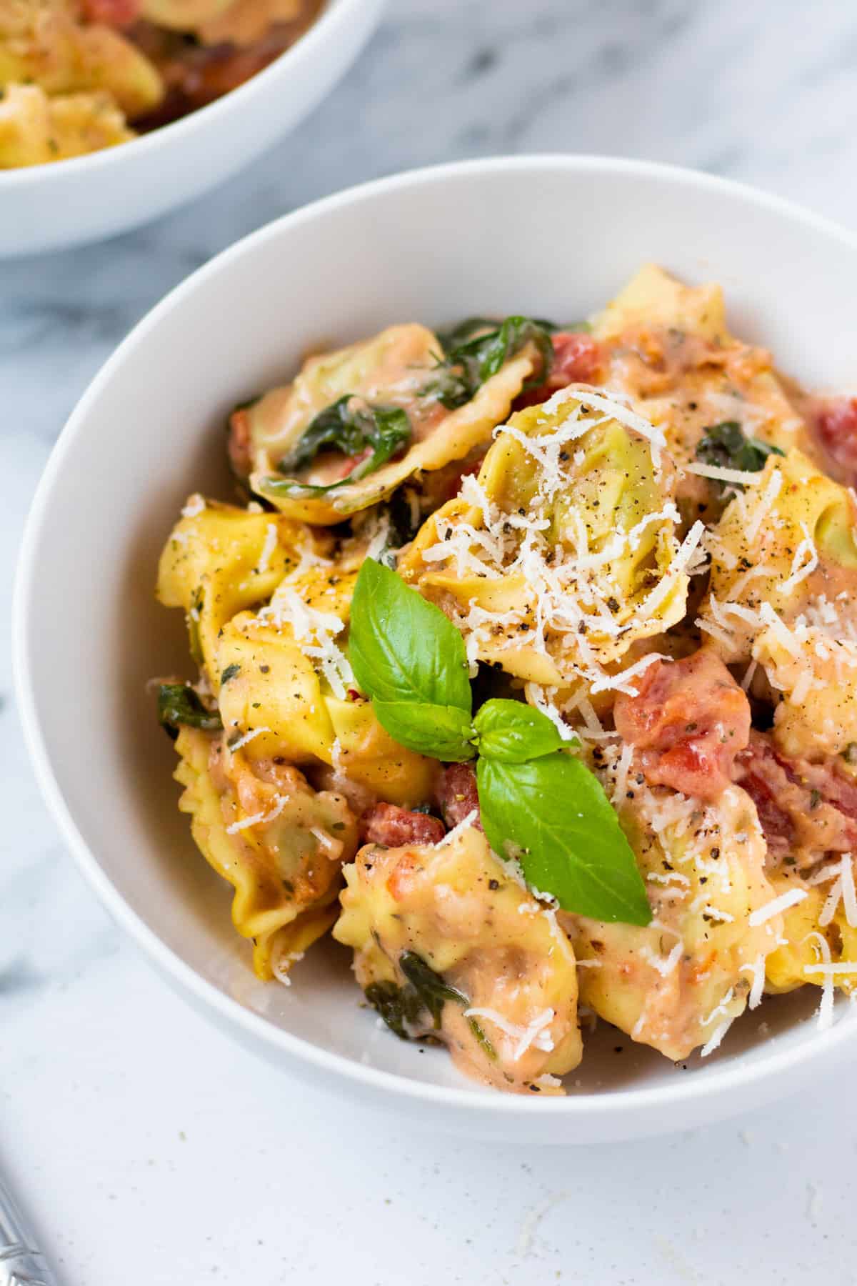 tomato and spinach cream sauce mixed with tortellini and topped with fresh basil and parmesan cheese in a white bowl