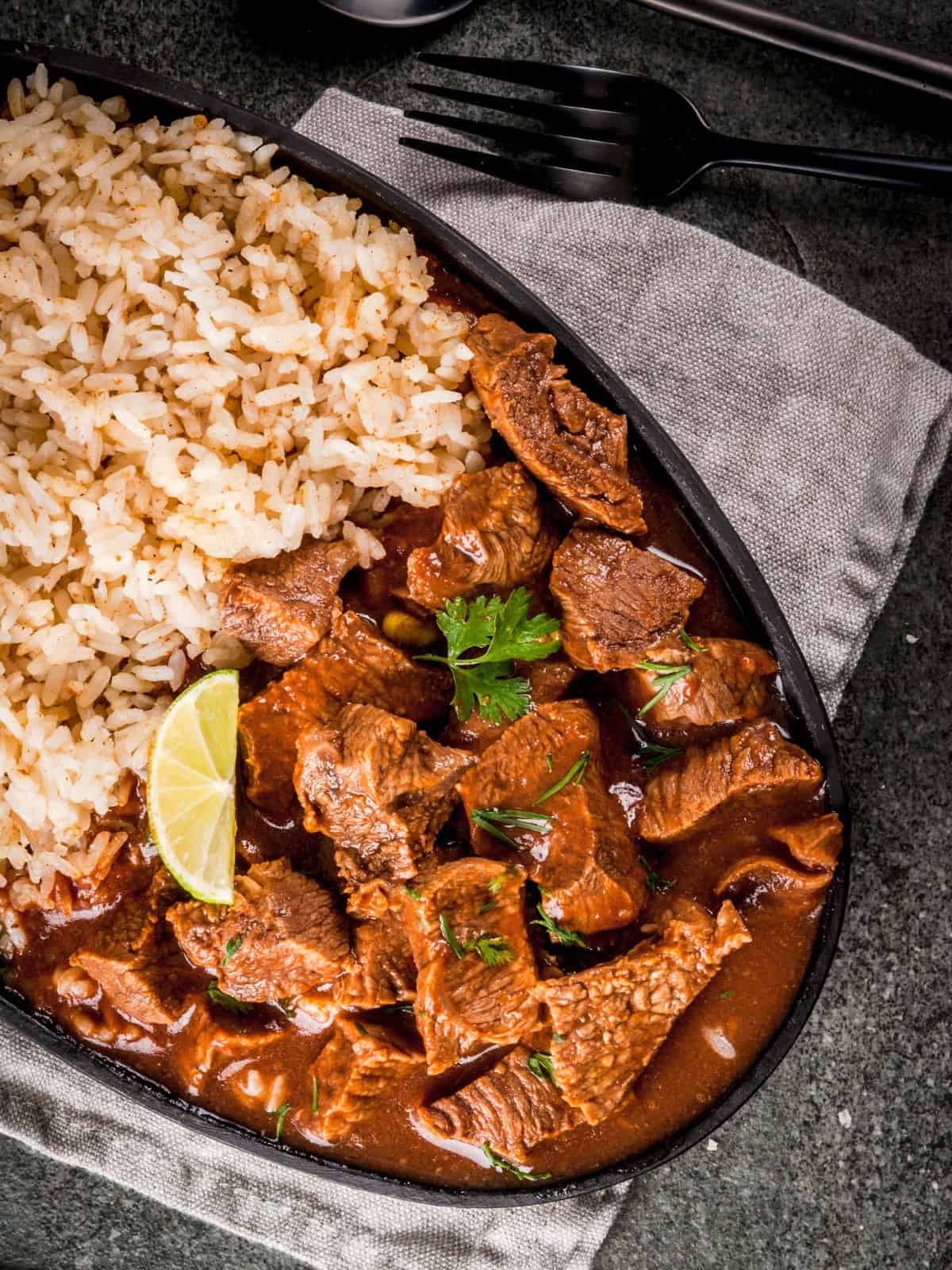 slow cooker chile rojo in a black bowl with Mexican rice