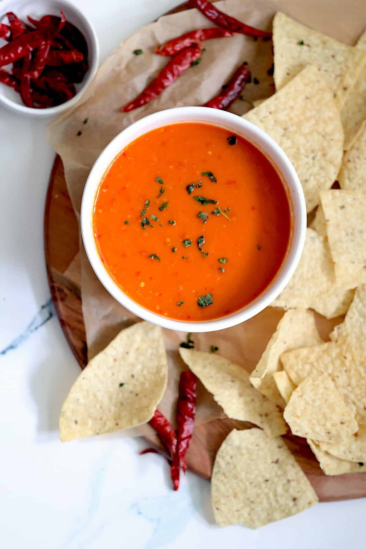 chile de arbol salsa in a white bowl surrounded by chips and peppers