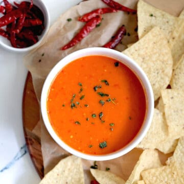 chile de arbol salsa in a white bowl surrounded by chips and peppers