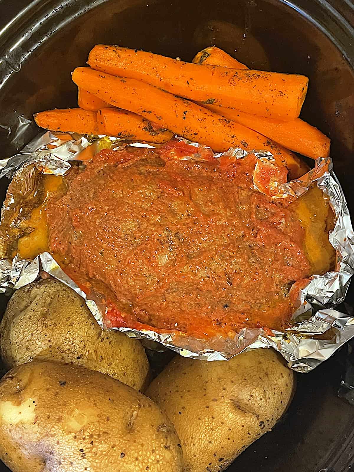 cooked meatloaf, potatoes and carrots in a slow cooker