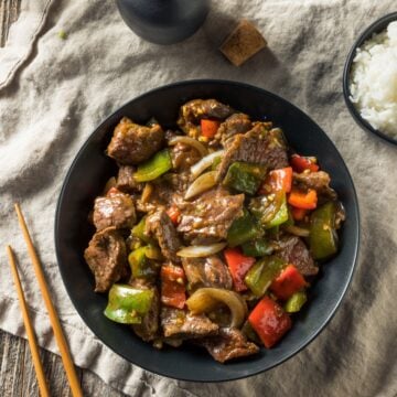 slow cooker pepper steak over rice in a black bowl