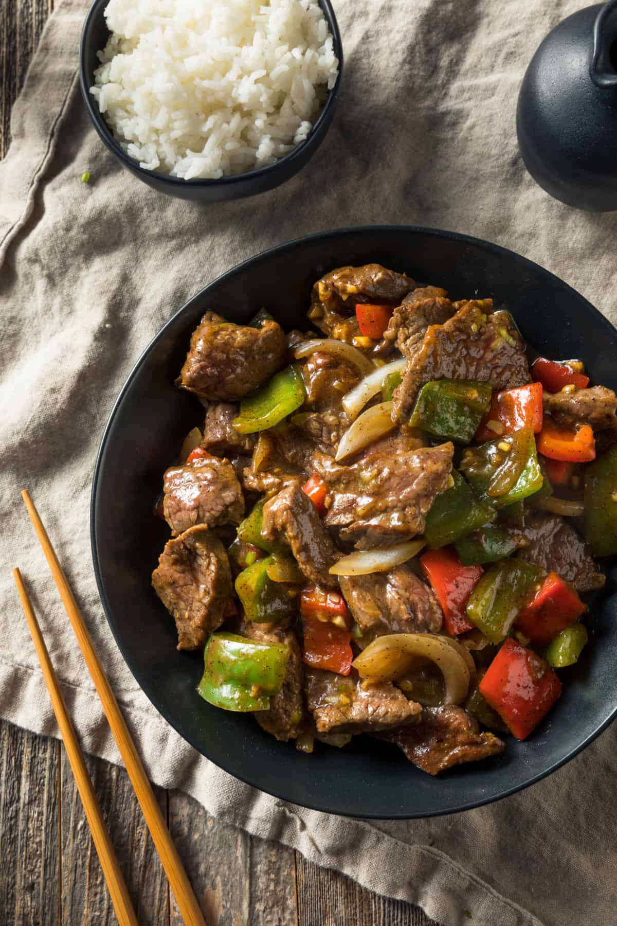 crockpot pepper steak in a black bowl served with white rice and chopsticks
