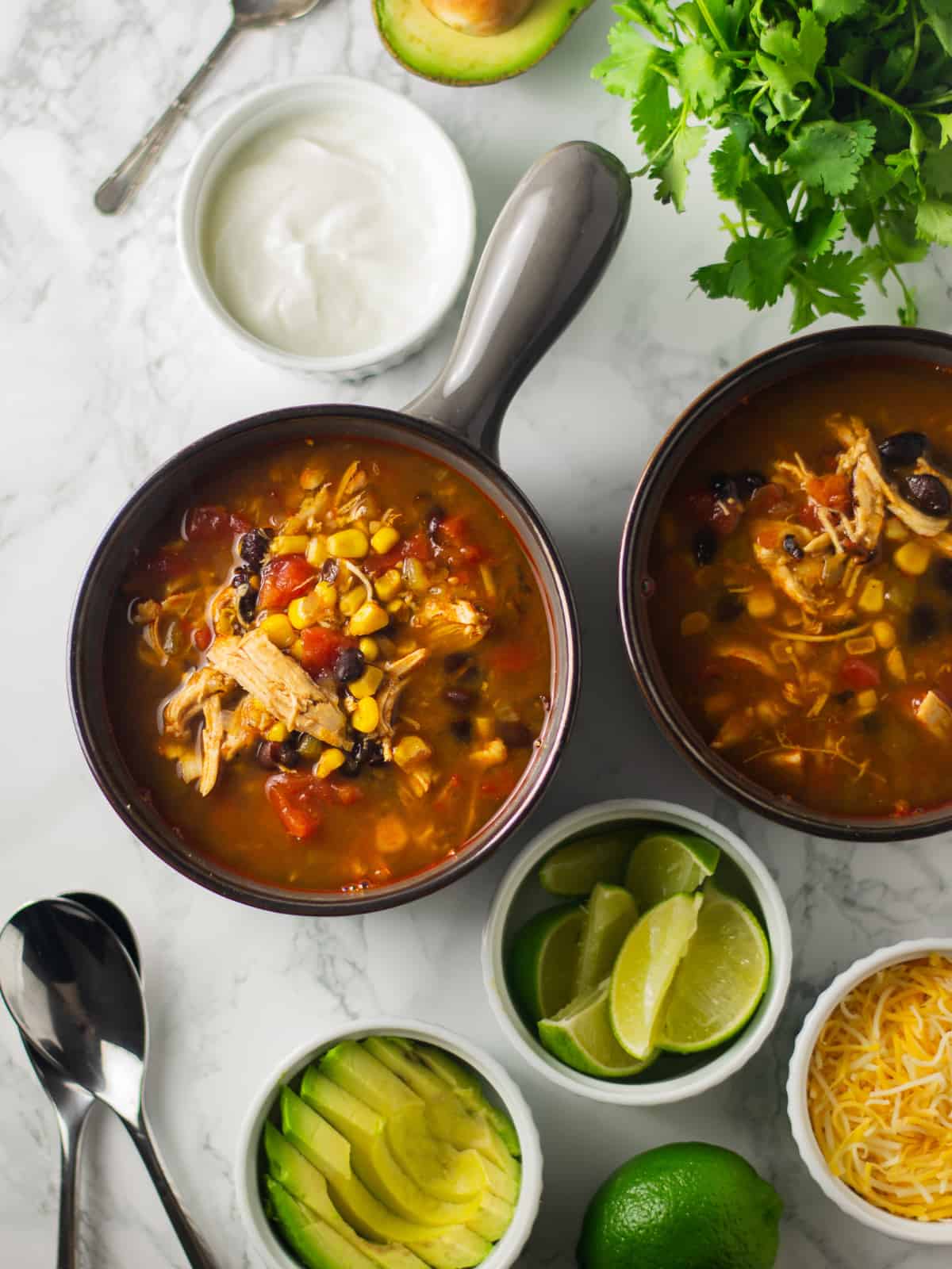 slow cooker taco soup in 2 black bowls with avocado, lime and cheese