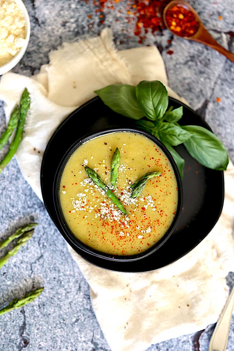 instant pot asparagus soup in black bowl with red pepper flakes, parmesan cheese and asparagus tips