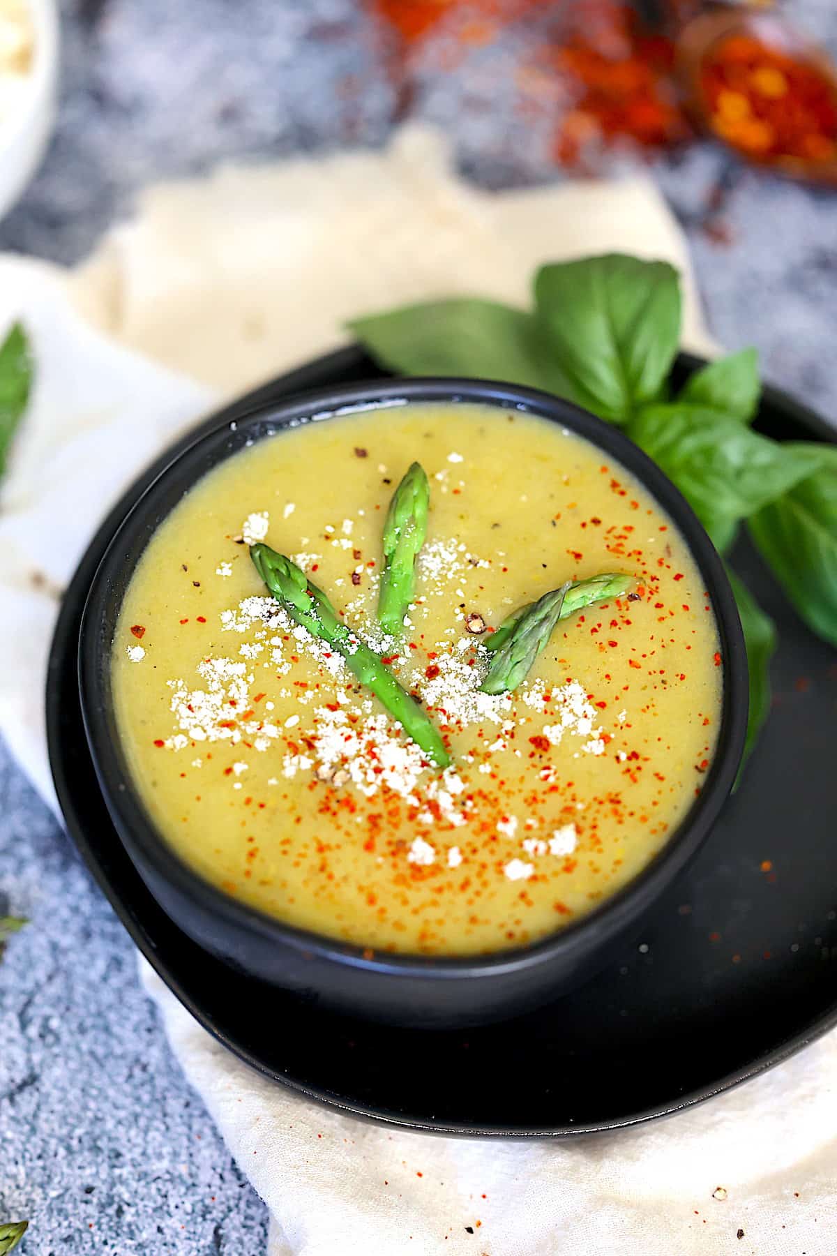 instant pot asparagus soup in black bowl with red pepper flakes, parmesan cheese and asparagus tips