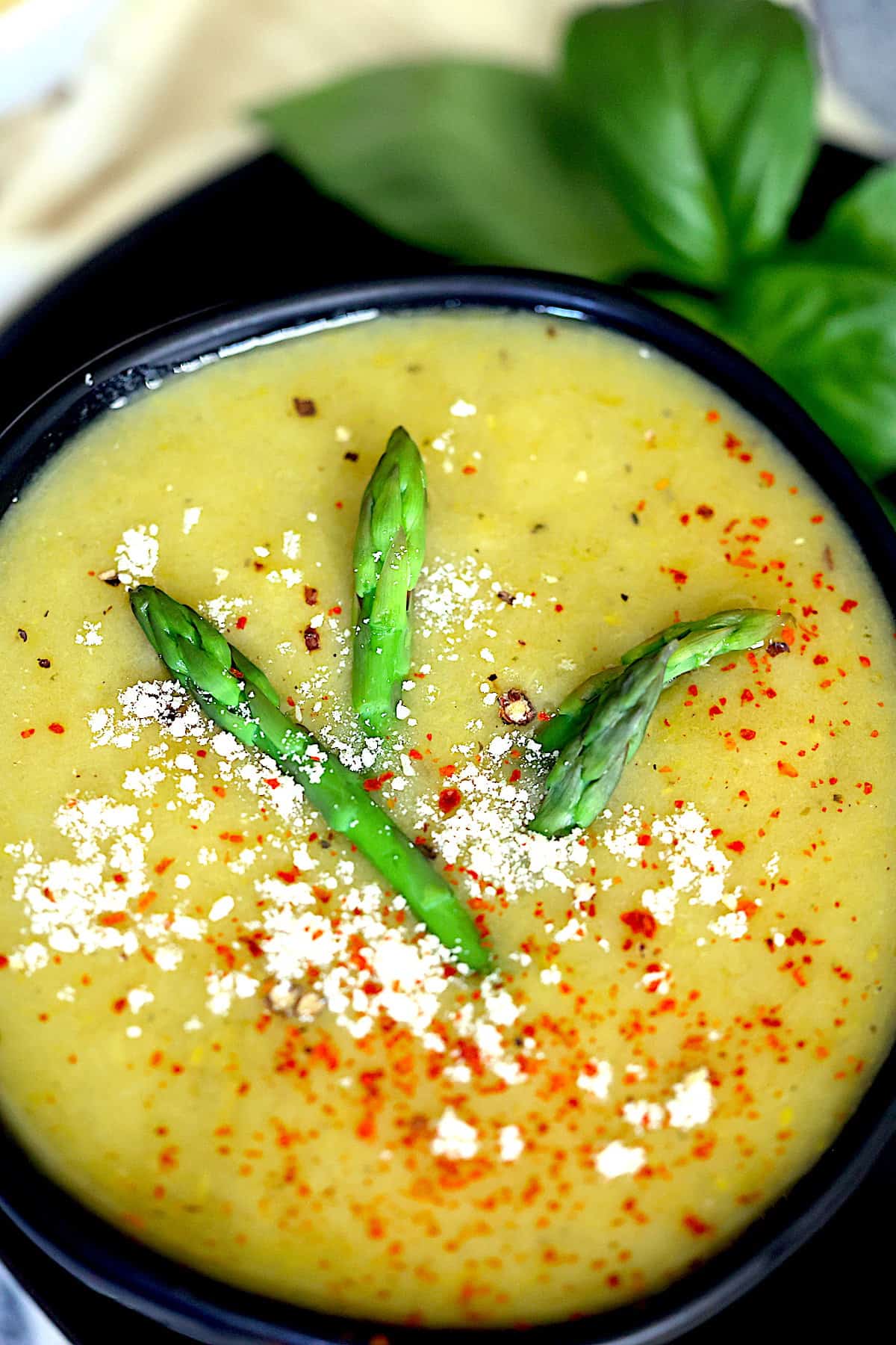 instant pot asparagus soup in a black bowl topped with parmesan cheese, red pepper flakes and asparagus tips