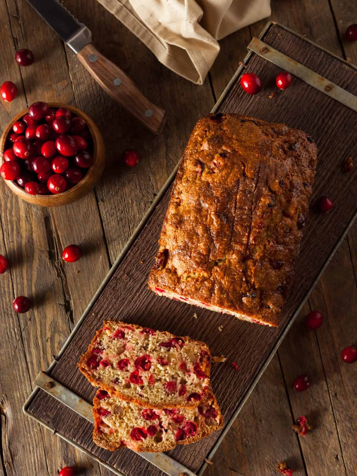 cranberry orange bread slices on a cutting board surrounded by fresh cranberries