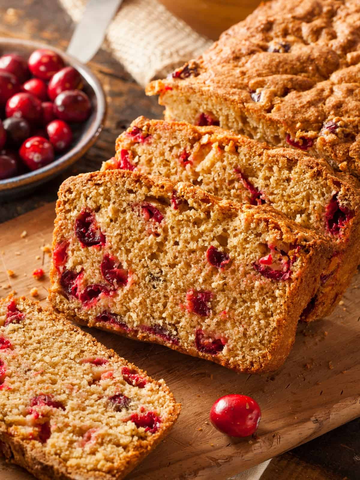 cranberry orange bread slices on a cutting board surrounded by fresh cranberries