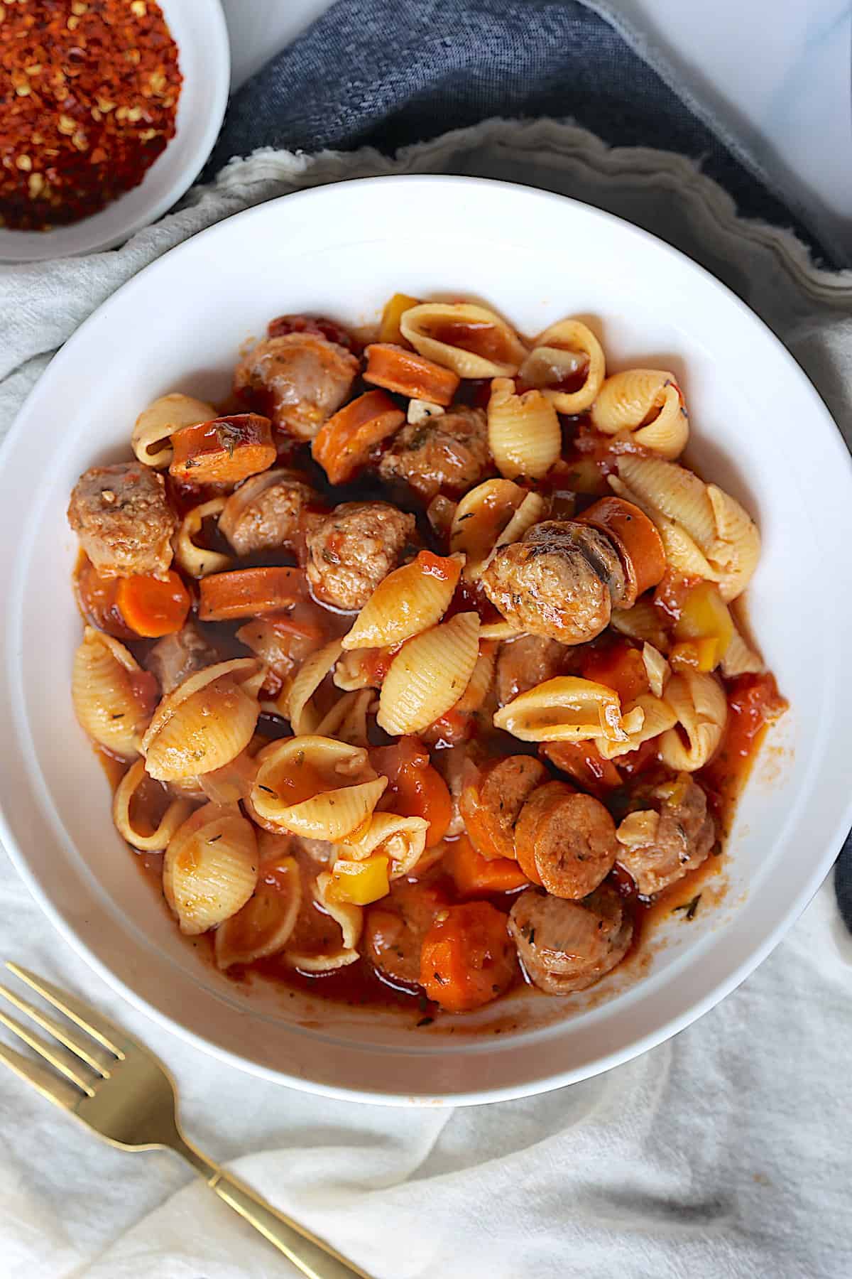 crock pot sausage stew in a white bowl with pasta shells