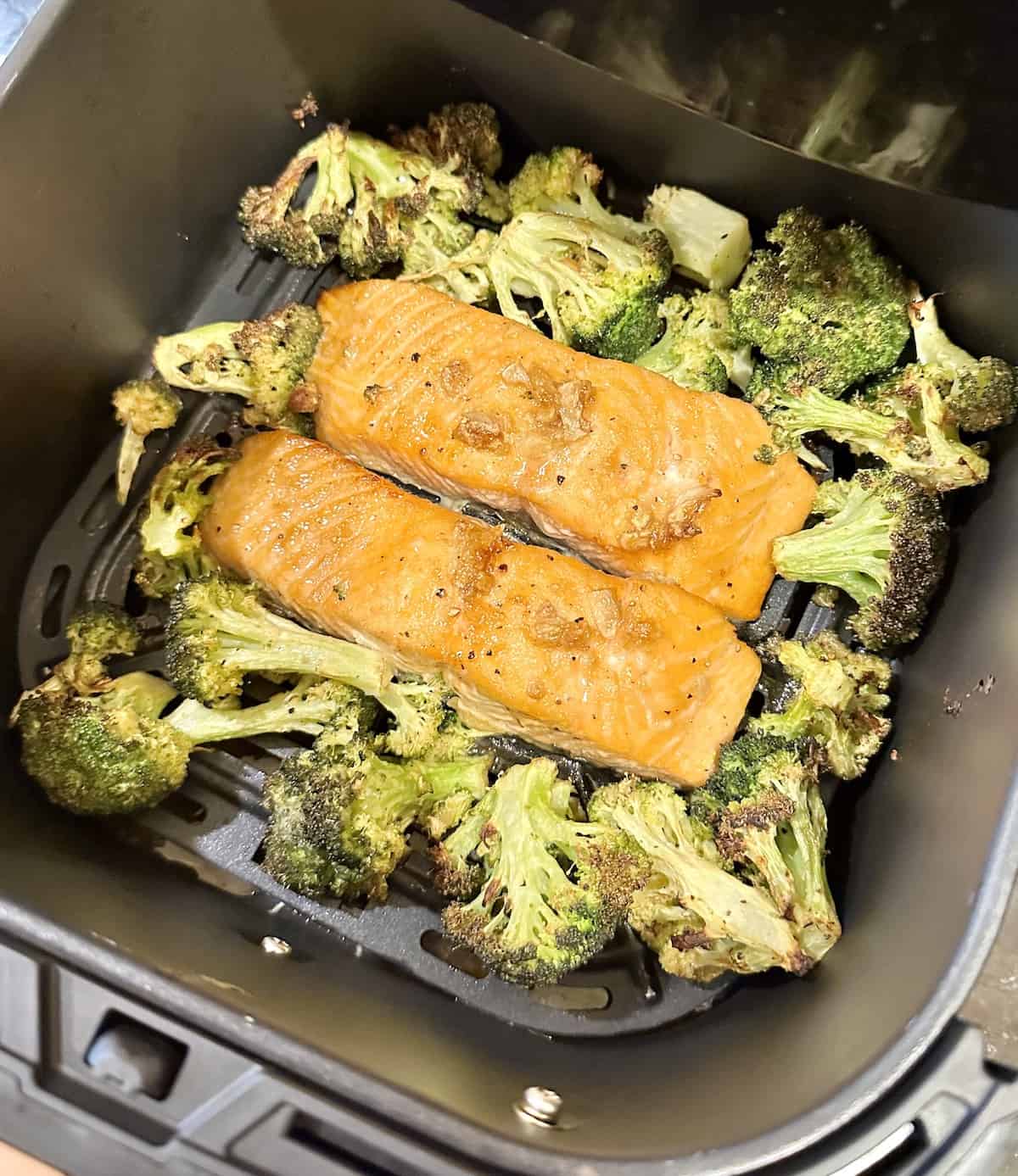 cooked salmon fillets and broccoli in an air fryer basket