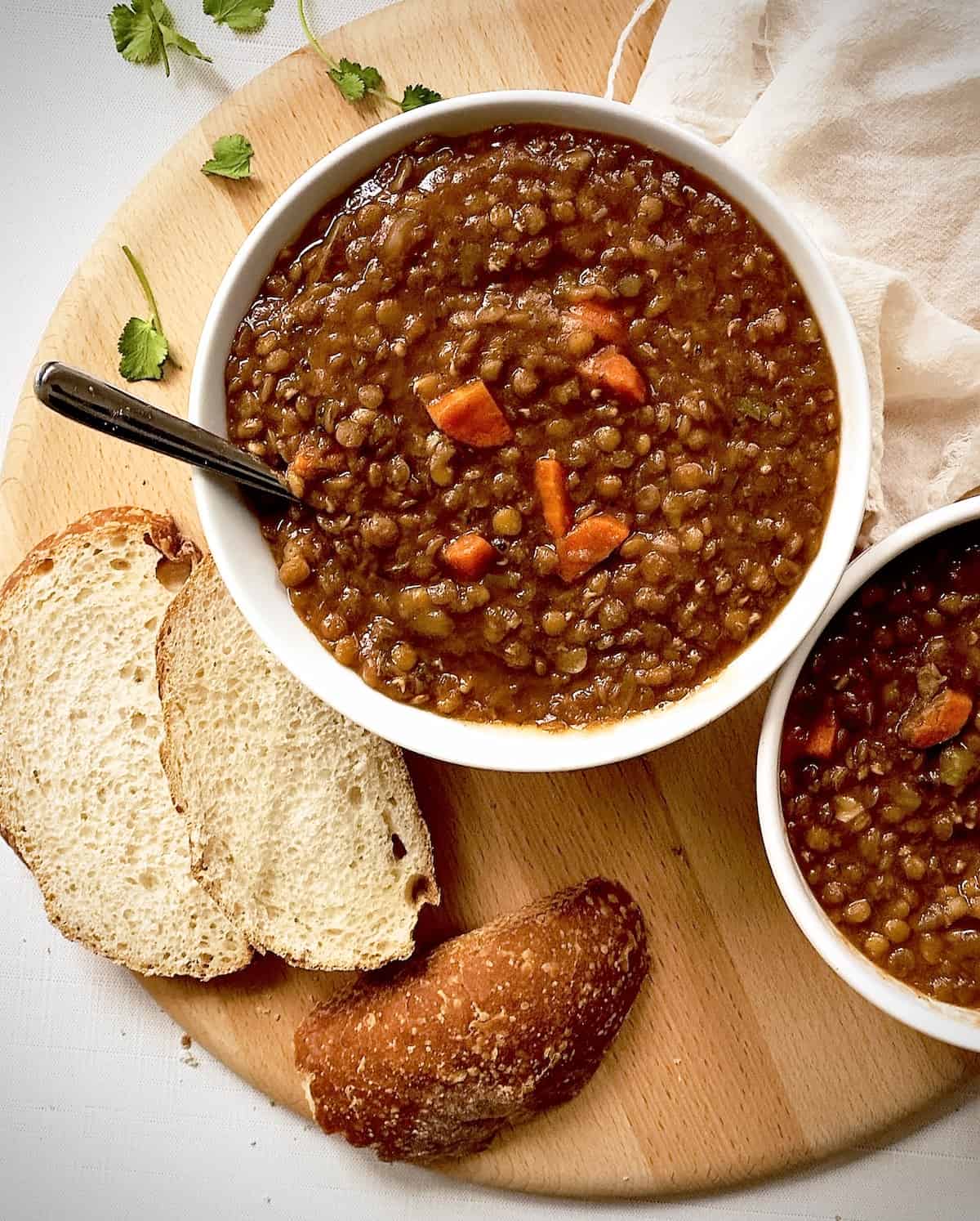 instant pot lentil soup in a white bowl on a wooden board with bread and herbs