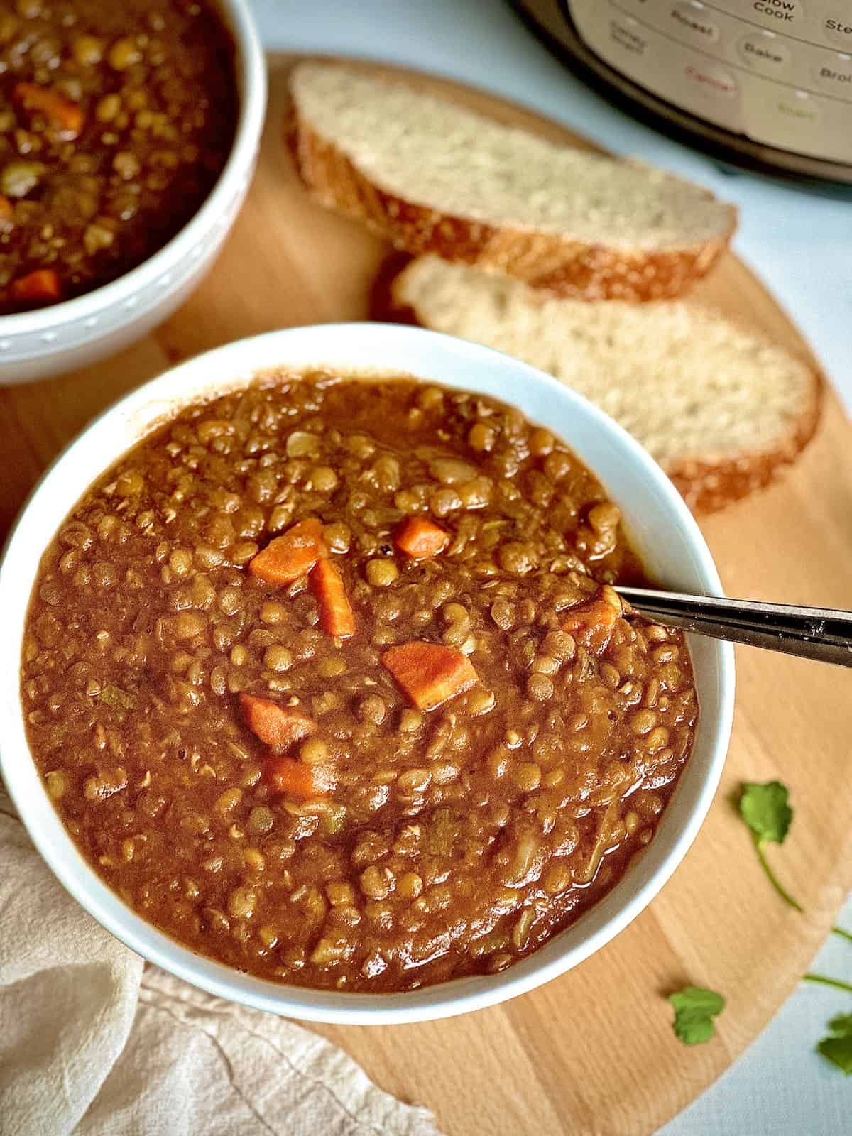 instant pot lentil soup in a white bowl on a wooden board with bread and herbs