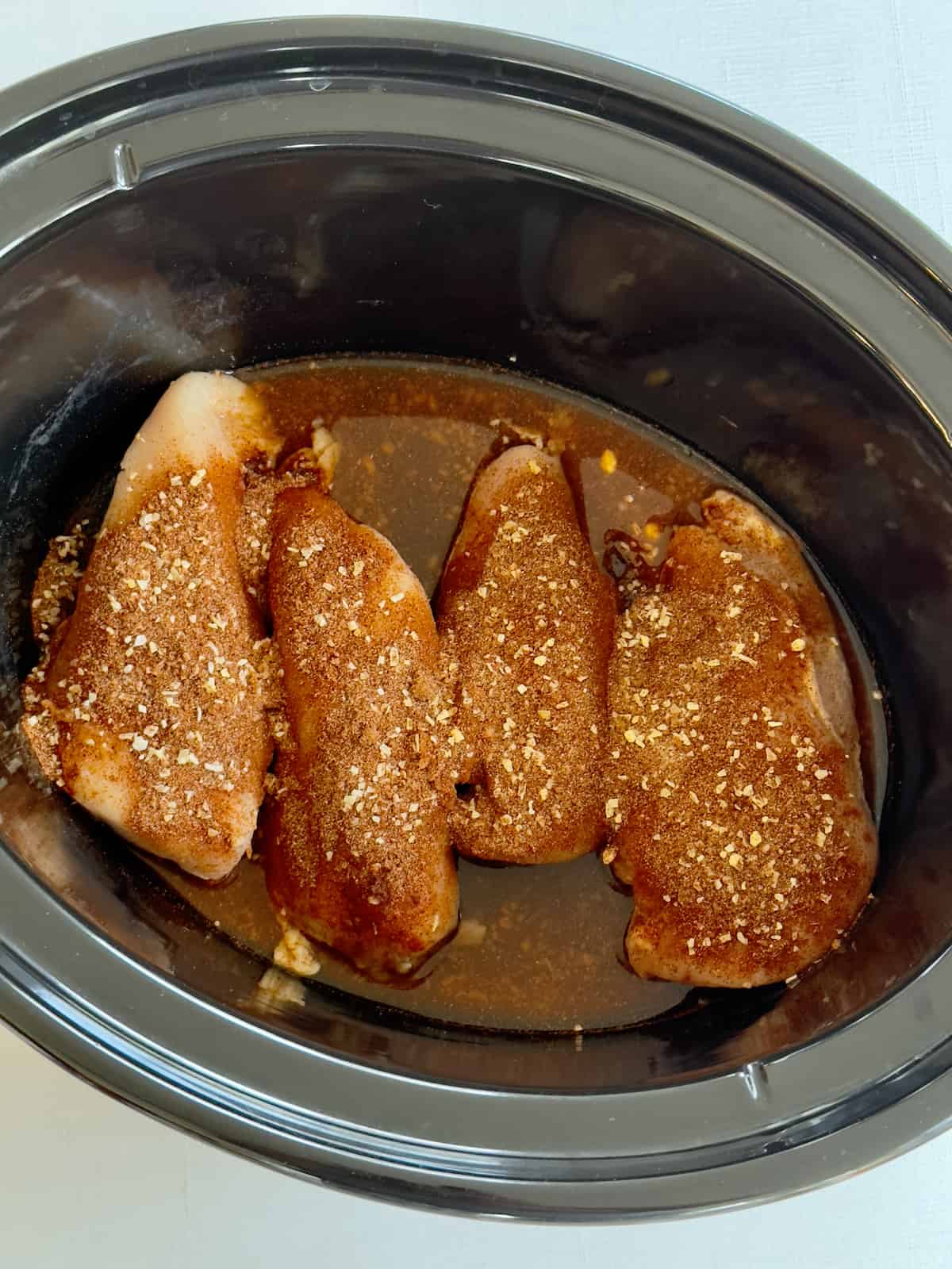 chicken breasts topped with seasonings and chicken broth in a crock pot