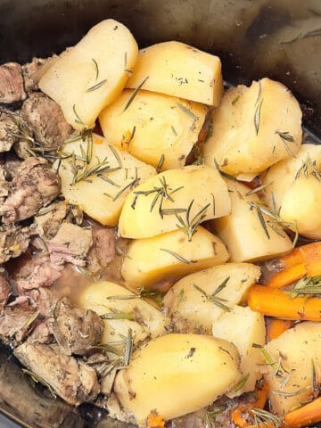 slow cooker lamb cubes in a crock pot with cut potatoes and carrots