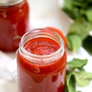 two mason jars of pressure cooked marinara sauce surrounded by fresh basil leaves
