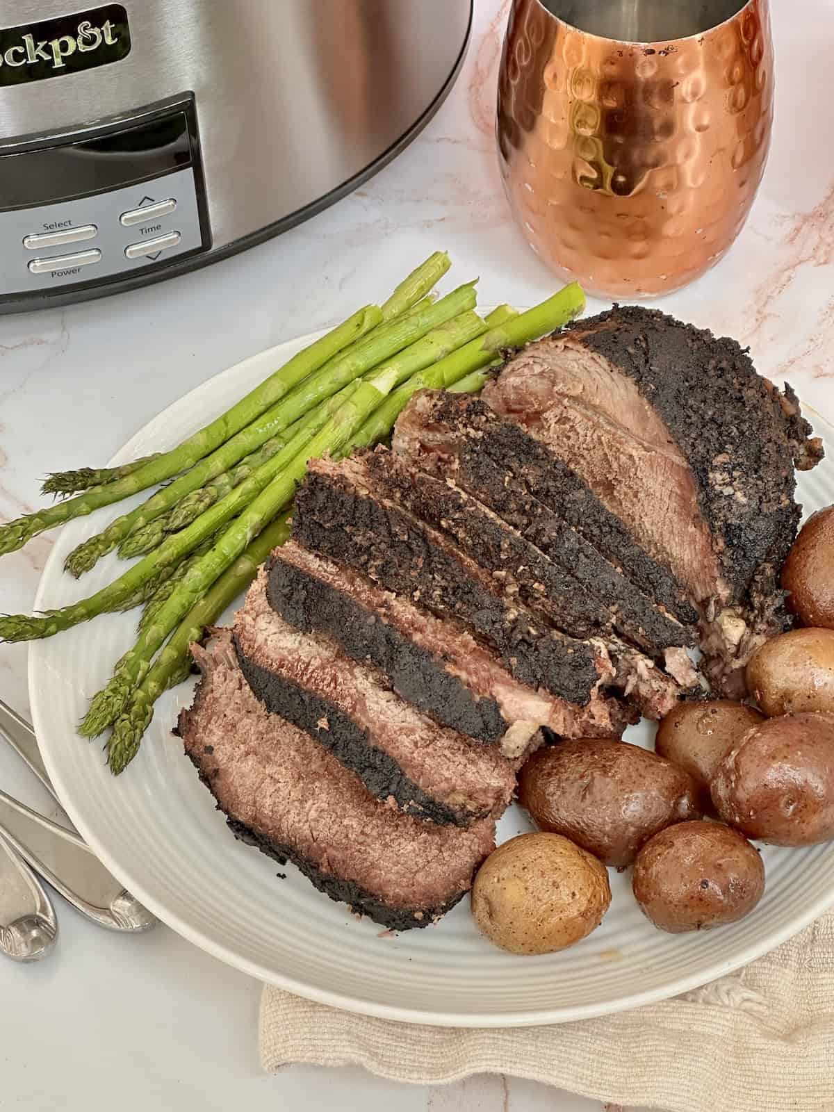 slow cooked tri tip roast sliced with potatoes and asparagus in a white plate