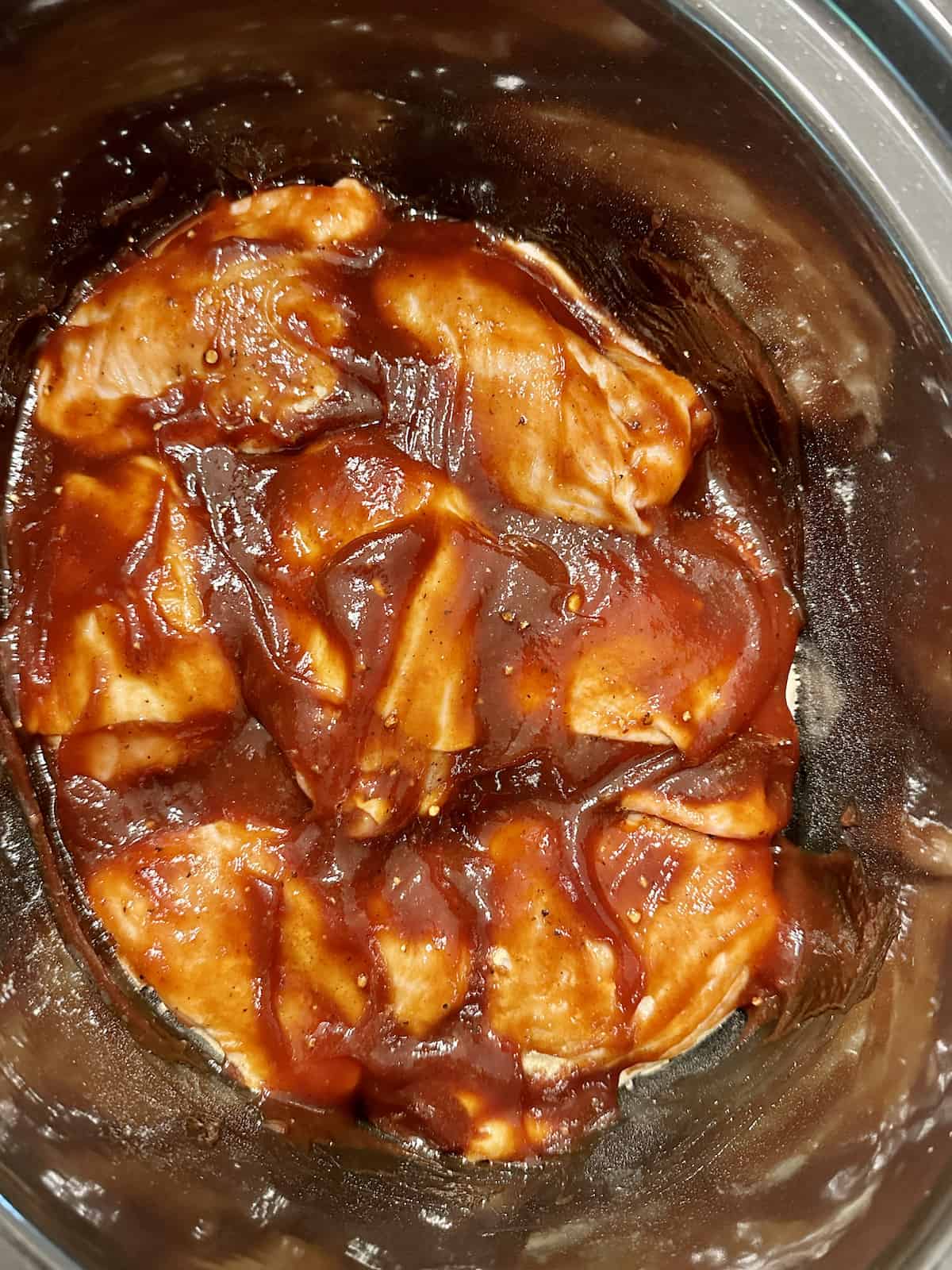 chicken thighs uncooked with bbq sauce in a slow cooker
