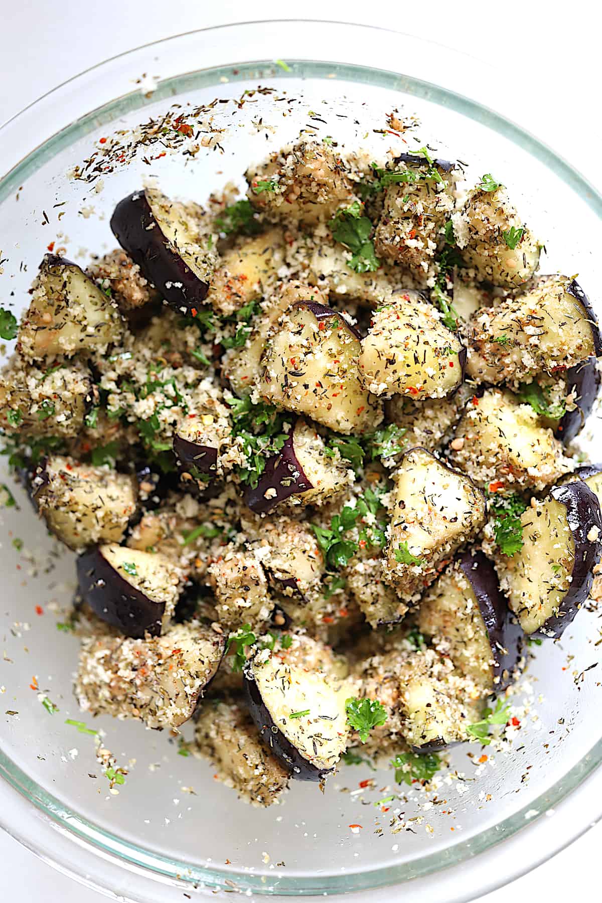 eggplant pieces in a mixing bowl tossed with herbs, oil and spices
