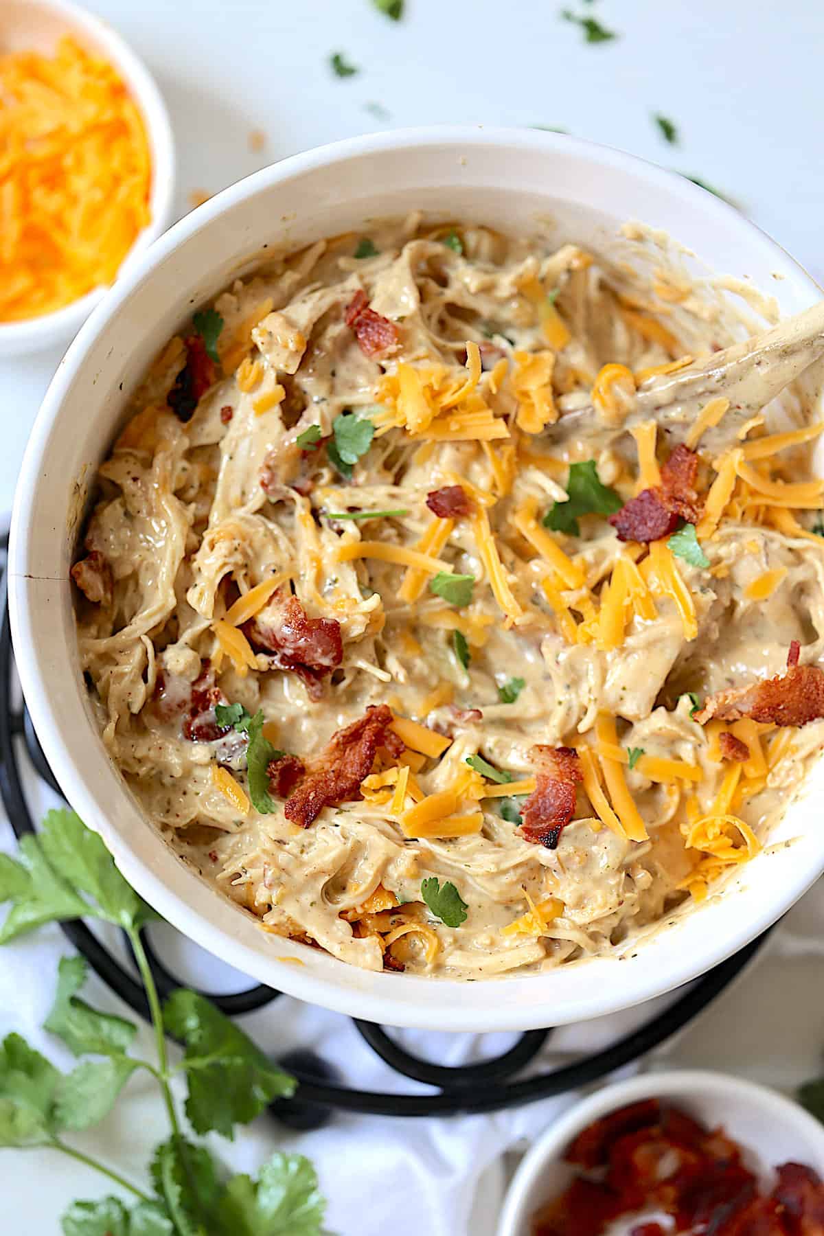 instant pot crack chicken in a white casserole dish with bacon and cilantro on top