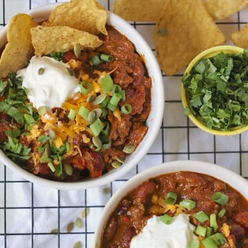 instant pot pumpkin chili in bowls topped with sour cream, cheese, cilantro and scallions