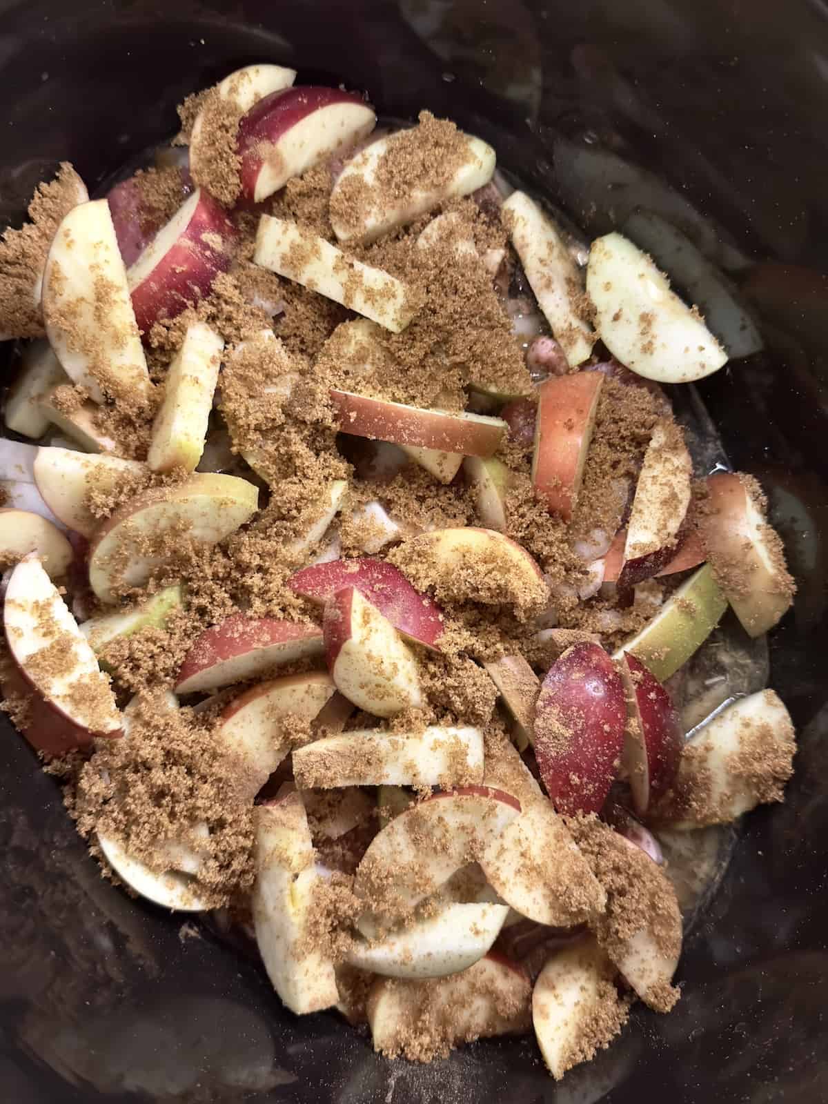apples, pork chops, onions and seasonings uncooked in a crock pot