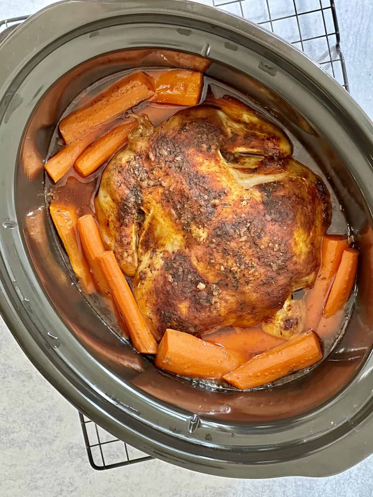 a seasoned whole chicken with carrots in a slow cooker