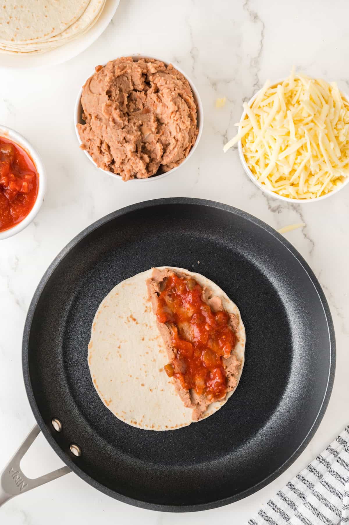 refried beans and salsa spread over a tortilla in a frying pan