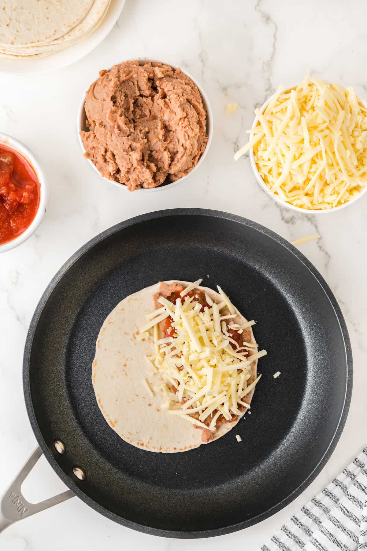 cheese, beans and salsa in a tortilla on a frying pan