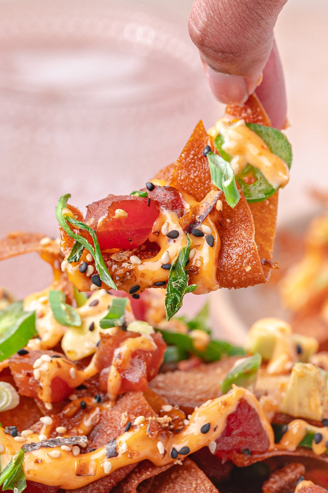 a piece of spicy tuna nachos on a chip being lifted off a place