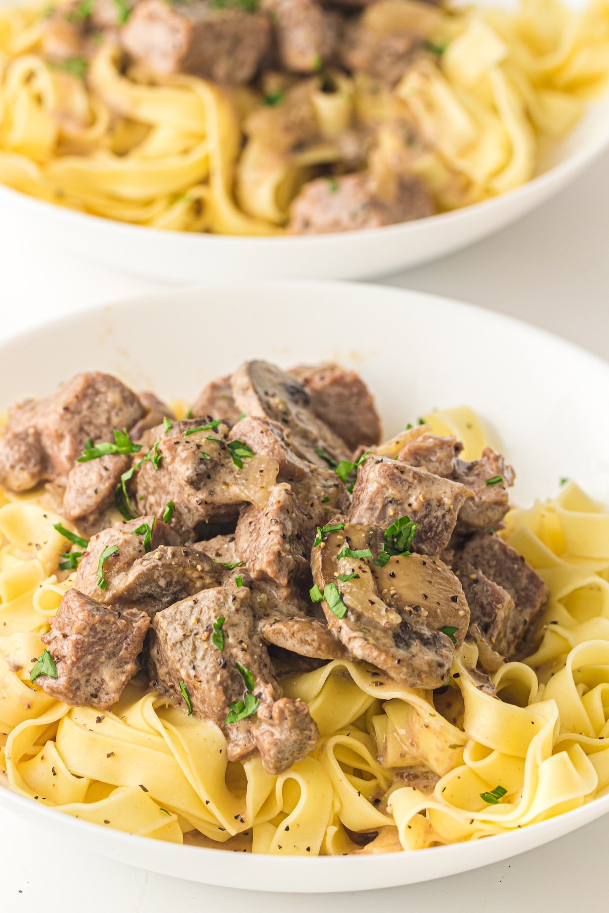 slow cooked beef stroganoff over noodles in a white plate