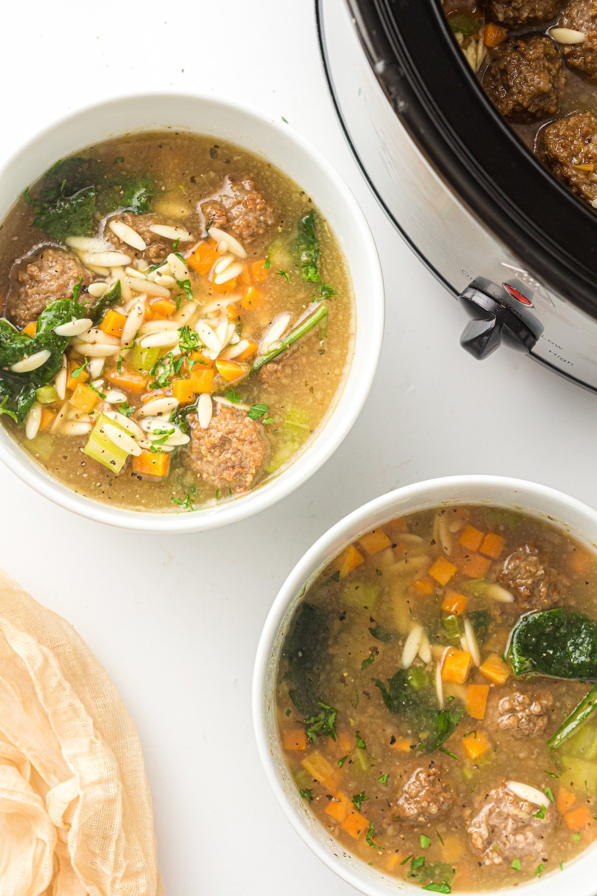 italian wedding soup in 2 white bowls and a crockpot
