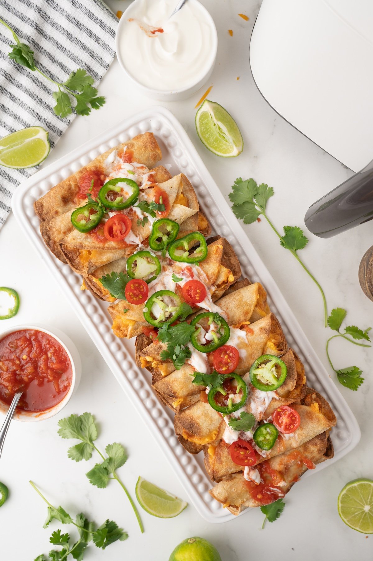 air fried refried bean taquitos topped with salsa, sour cream and jalapenos on a white plate