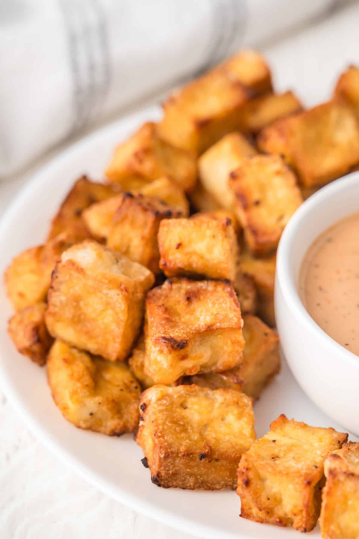 crispy air fryer tofu nuggets on a white plate with dipping sauce