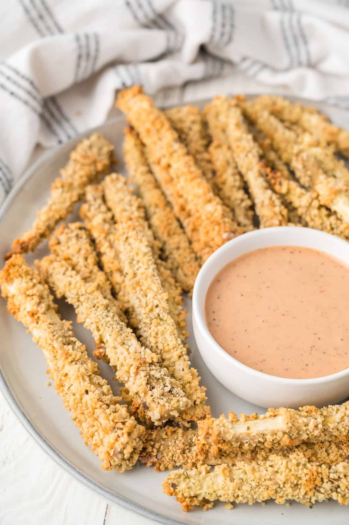 crispy golden zucchini fries on a white plate with dipping sauce