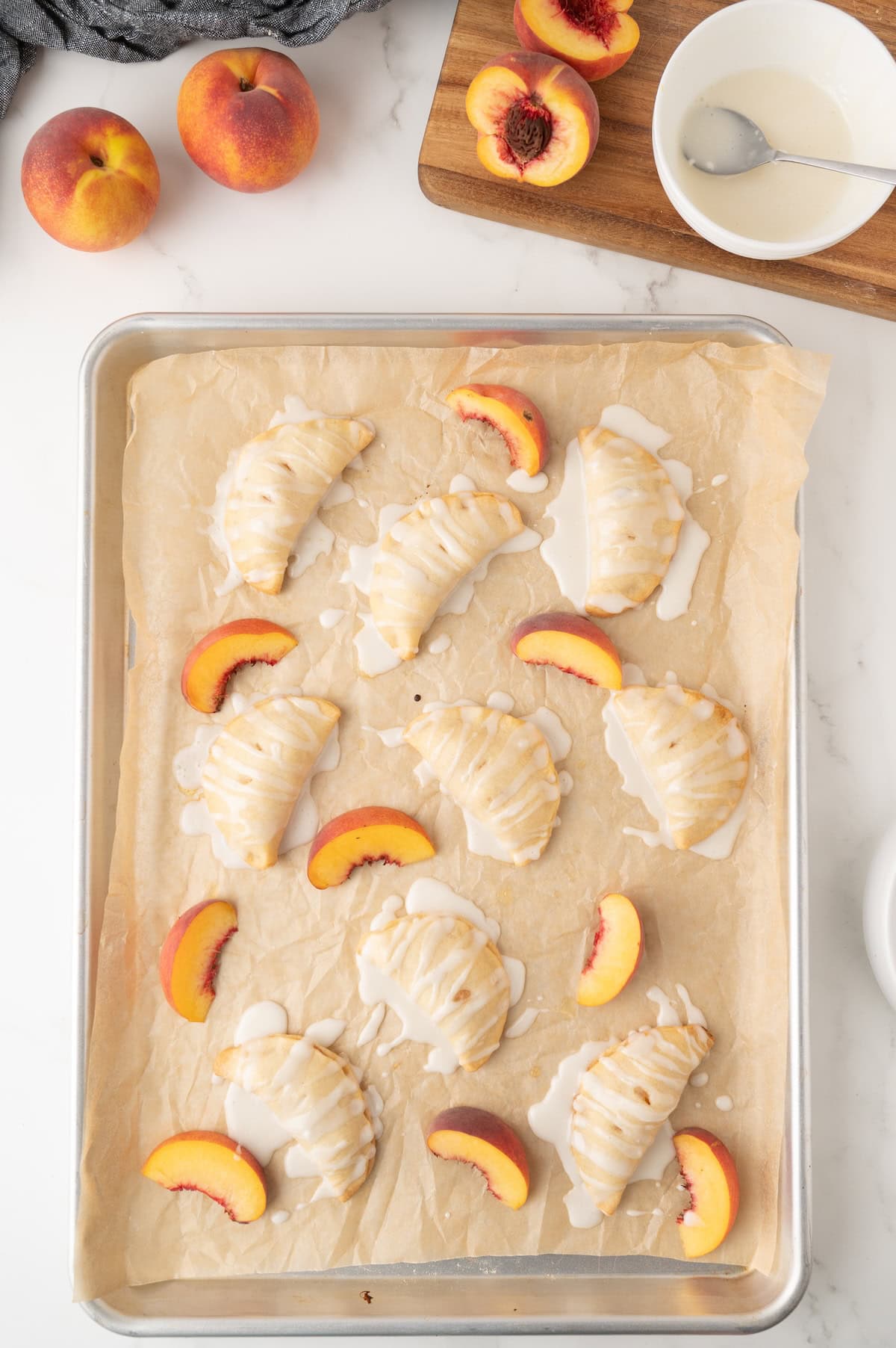 cooked mini peach hand pies on a baking sheet topped with glaze