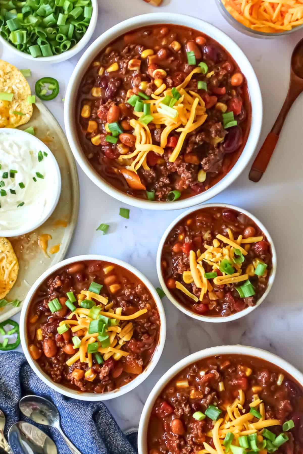 slow cooked beef chili in white bowls topped with cheese and scallions