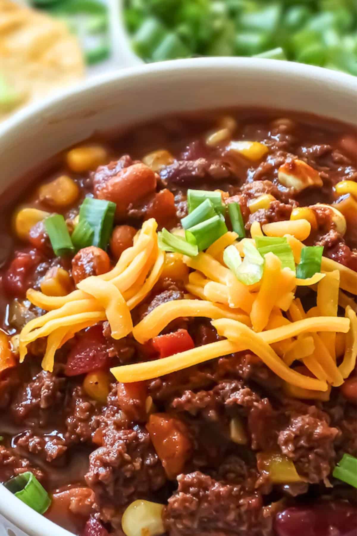 close up of crockpot beef and bean chili in a bowl with toppings