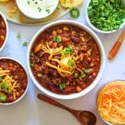 slow cooker beef and bean chili in serving bowls topped with cheddar cheese and scallions