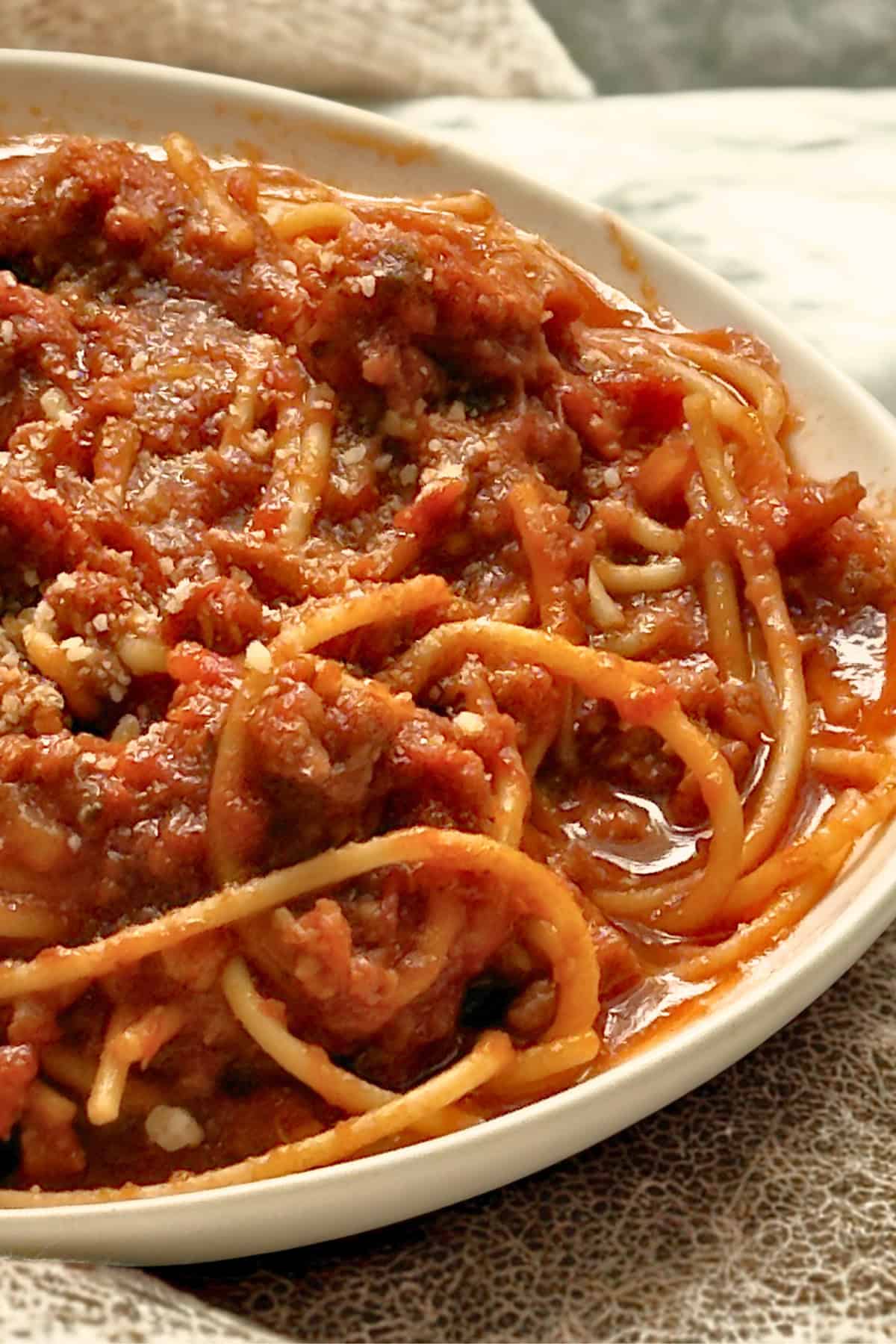 plate of spagheti and meat sauce topped with parmesan cheese